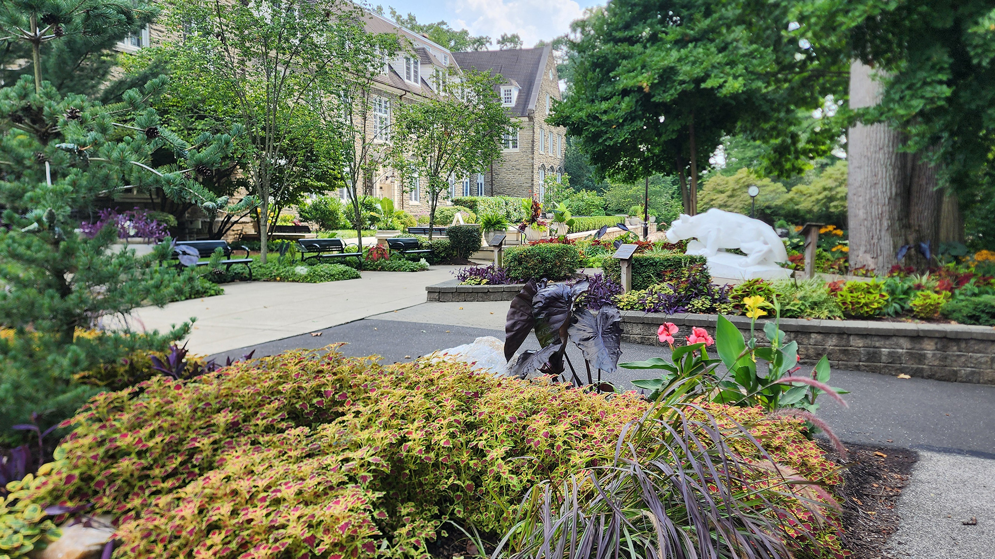 The Penn State Abington campus in August, showing a stone building and the lion shrine surrounded by lush greenery.